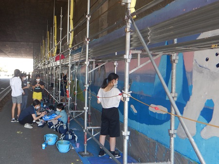 A photograph of the art club students at Takasaki Municipal Nakao Junior High School building scaffolds and painting a mural