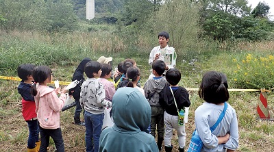 Photograph of biotope explanation to elementary school students (near Akiruno IC on the Ken-Ken-O Road Expressway)