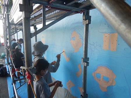 高崎市立新高尾小学校の生徒さんたちが保護者と壁画を描いているの写真